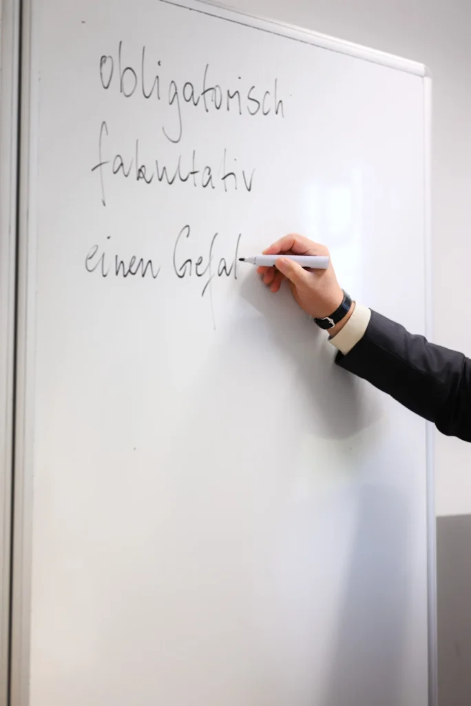 Hand schreibt Grammatikbegriffe an das Whiteboard im Deutschunterricht bei LECTOR